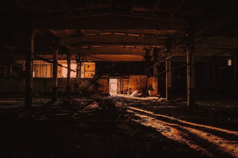 Dark abandoned factory hall with industrial beams and warm light