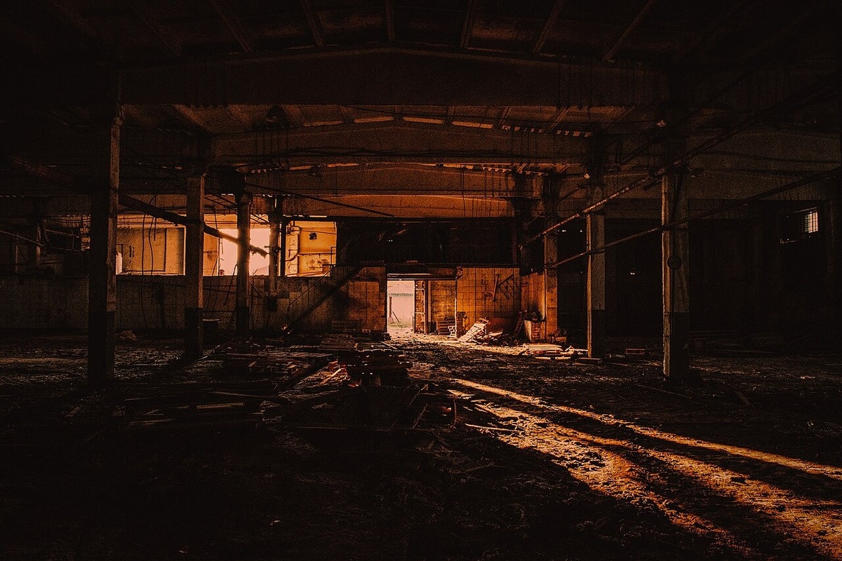 Dark abandoned factory hall with industrial beams and warm light